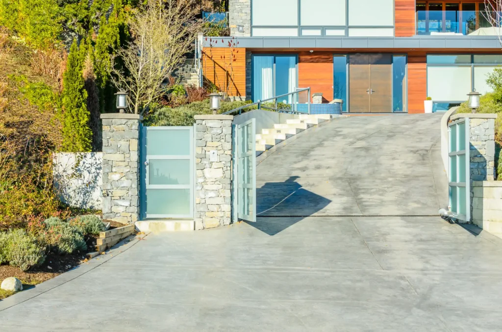 A modern house with large windows, a wooden facade, and a wide sealcoat driveway Iowa residents admire, complete with a partially open metal and glass gate.